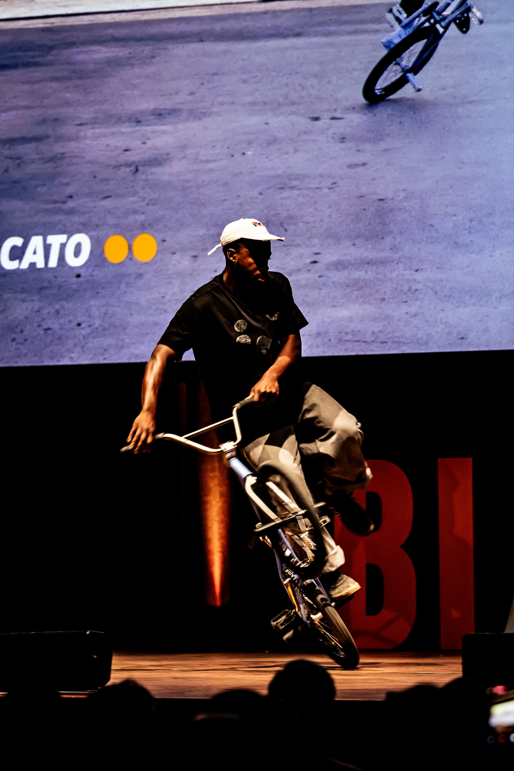 Omari Cato performing a flatland BMX trick on stage during a Bike Film Tour event.