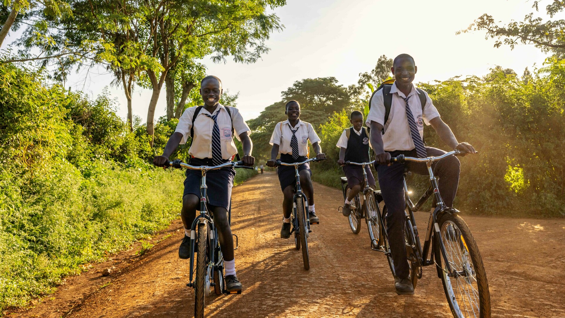 Group of students in school uniforms riding bicycles on a dirt road.